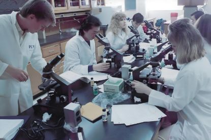 Students in white lab coats working with microscopes